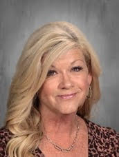 Portrait of a smiling woman with long, blonde hair, wearing a leopard-print top and a necklace. Background is gray.