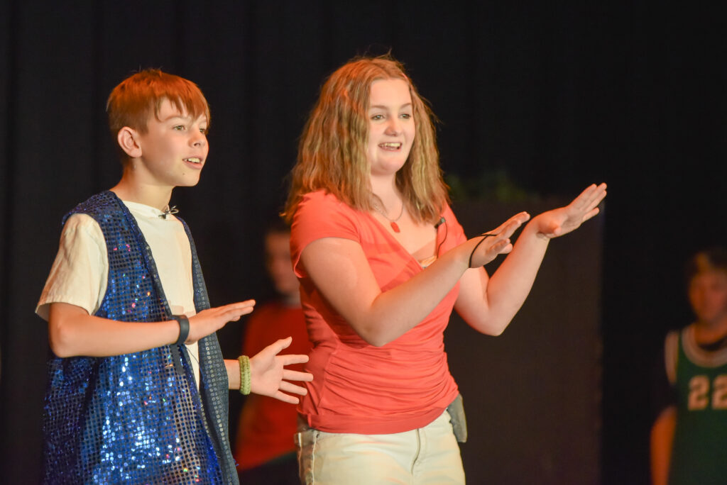 Male student standing to the left of a female student on stage with jazz hands in front of their bodies. 