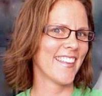 Smiling woman with glasses and medium-length brown hair, wearing a green shirt against a blurred background.
