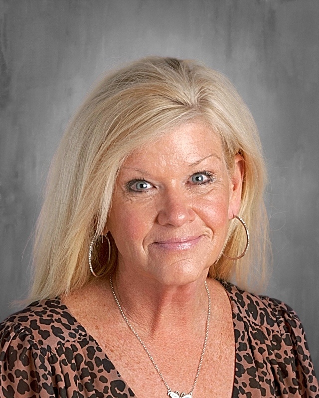 Smiling woman with long blonde hair, wearing leopard print top and hoop earrings, against a gray background.