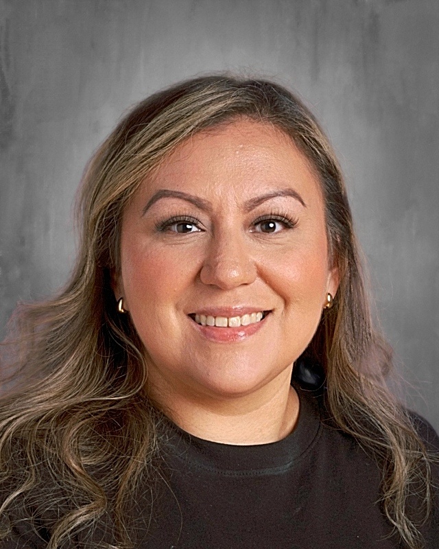 Smiling person with long hair and earrings against a gray background.
