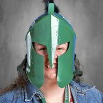 Una persona que lleva un casco espartano verde y una chaqueta vaquera, con una amplia sonrisa.