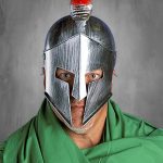 Persona que lleva un casco plateado con un penacho rojo y una capa verde, sobre un fondo gris.
